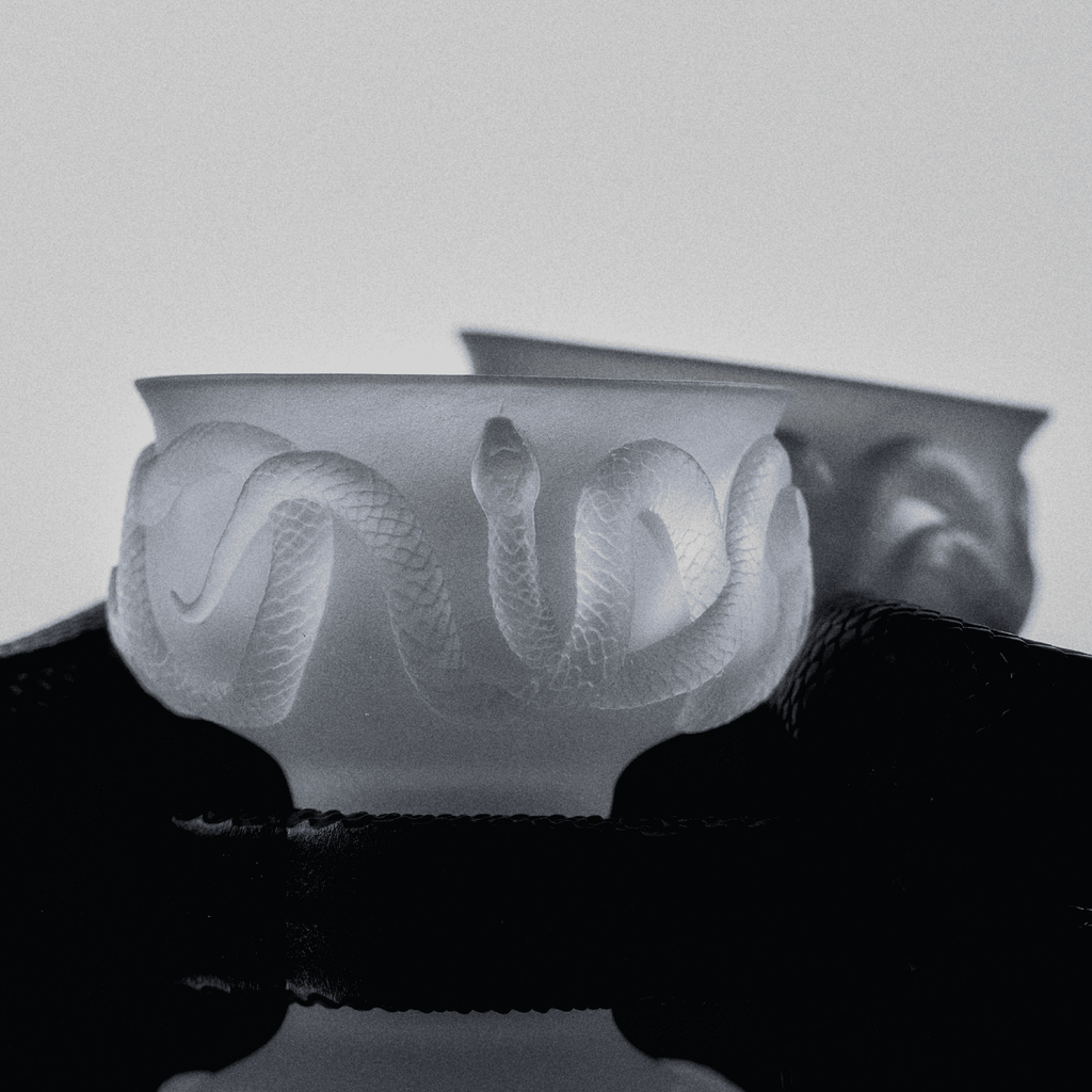 Close-up of relief glaze glass tea cup showing serpent scale texture and carved ebony coaster detail