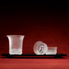 Set of frosted glass cups on a black tray against a red background