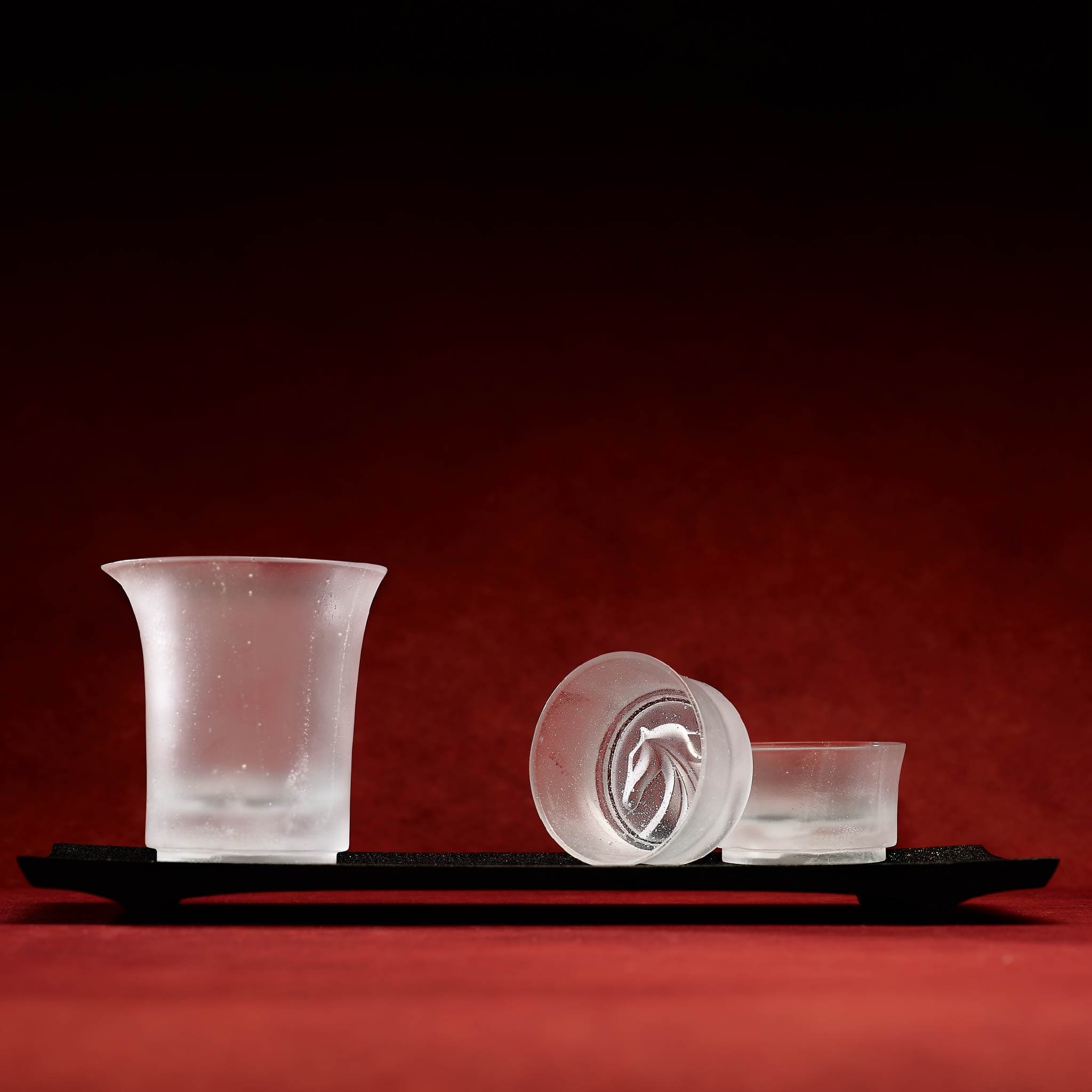 Set of frosted glass cups on a black tray against a red background