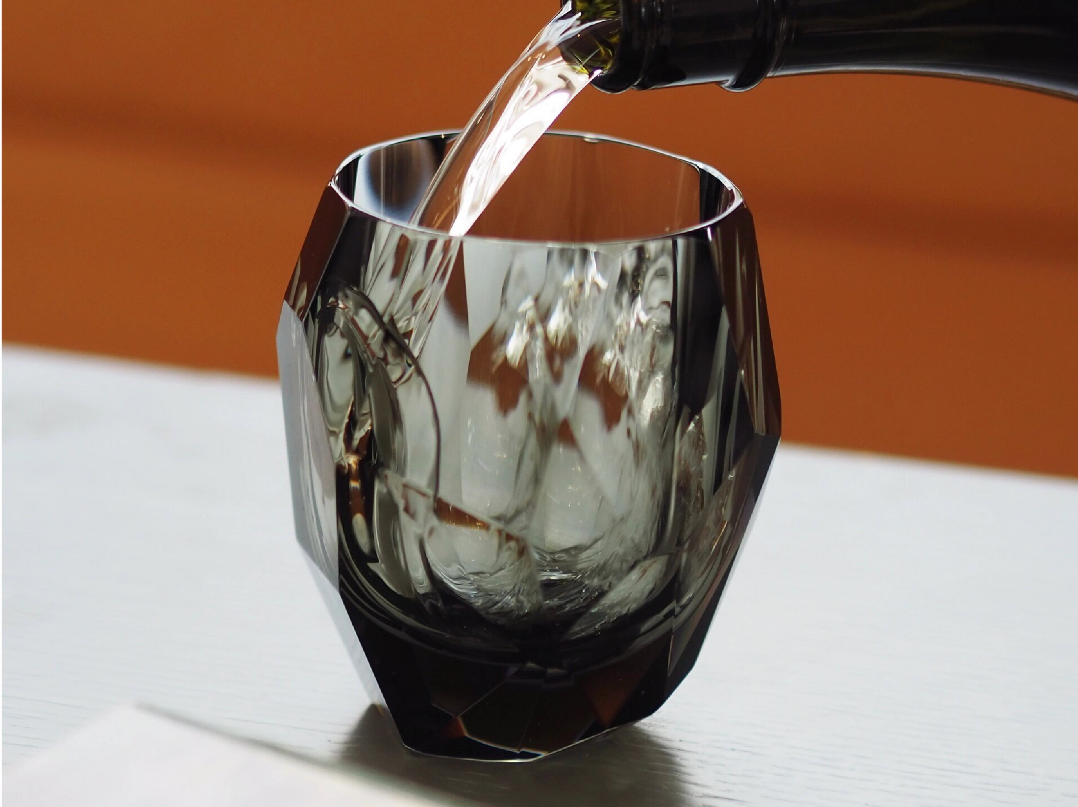 Close-up of crystal whiskey glass showing polygonal gemstone-like facets, polished edges, and thick weighted base