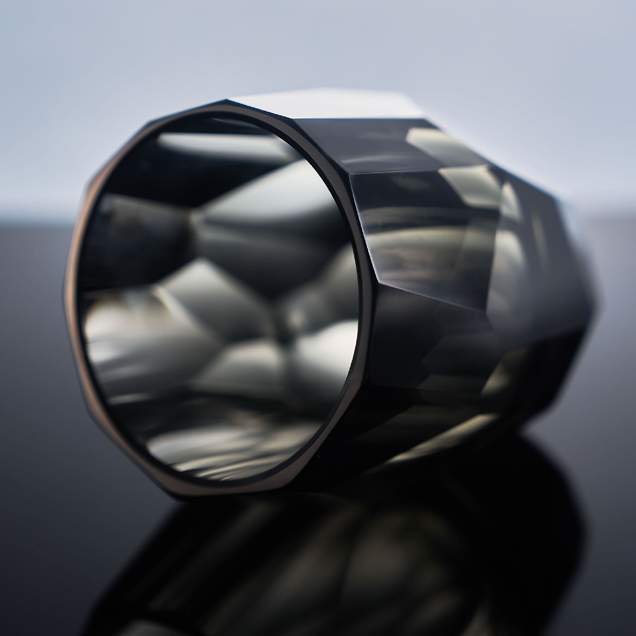 Close-up of crystal whiskey glass showing polygonal gemstone-like facets, polished edges, and thick weighted base